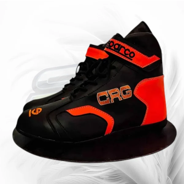 A black and bright orange high-top racing shoe with 'sparco' branding on the ankle strap and 'CAG' on the side, shown against a white background with a faint gray racing stripe graphic.